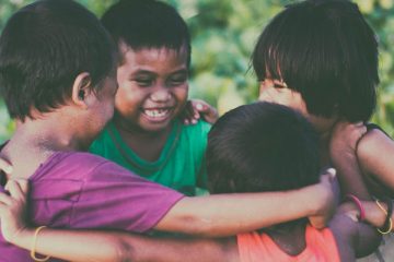 Cuatro niños sonriendo y abrazándose en círculo que ilustran la importancia de educar en la No violencia