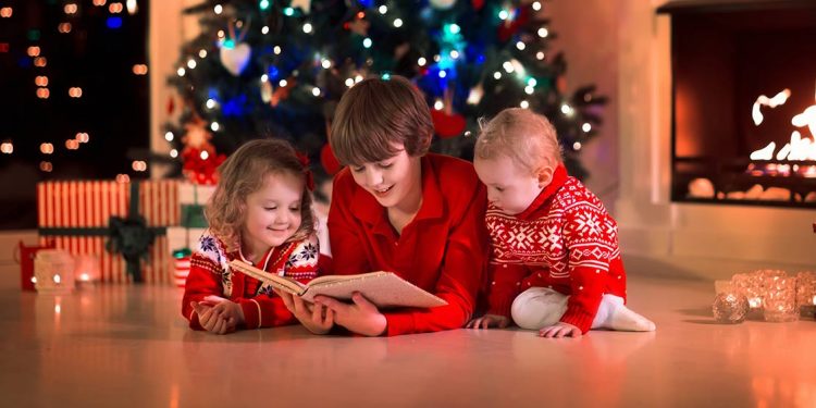 Tres niños leyendo con un árbol navideño de fondo para ilustrar las 10 recomendaciones de libros para estas navidades