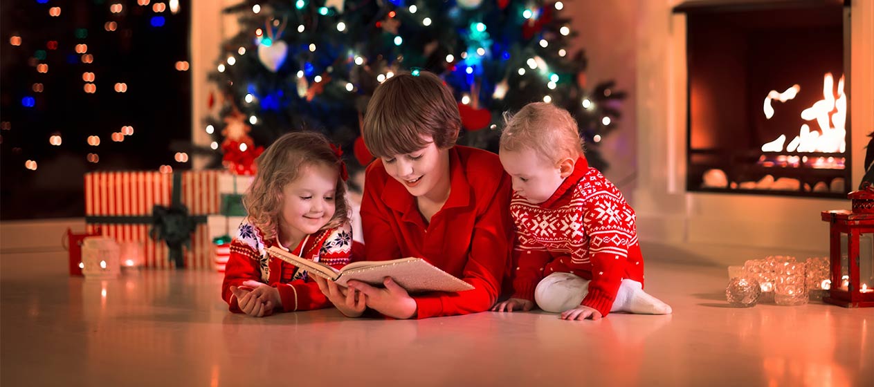 Tres niños leyendo con un árbol navideño de fondo para ilustrar las 10 recomendaciones de libros para estas navidades