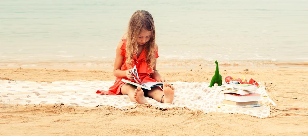 niña leyendo en la playa una lectura para estas vacaciones