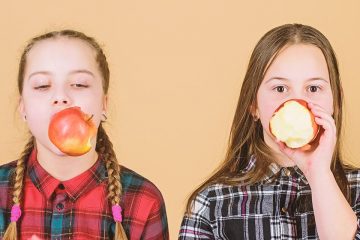 Dos nenes amb una poma a la boca per il·lustrar els bons hàbits