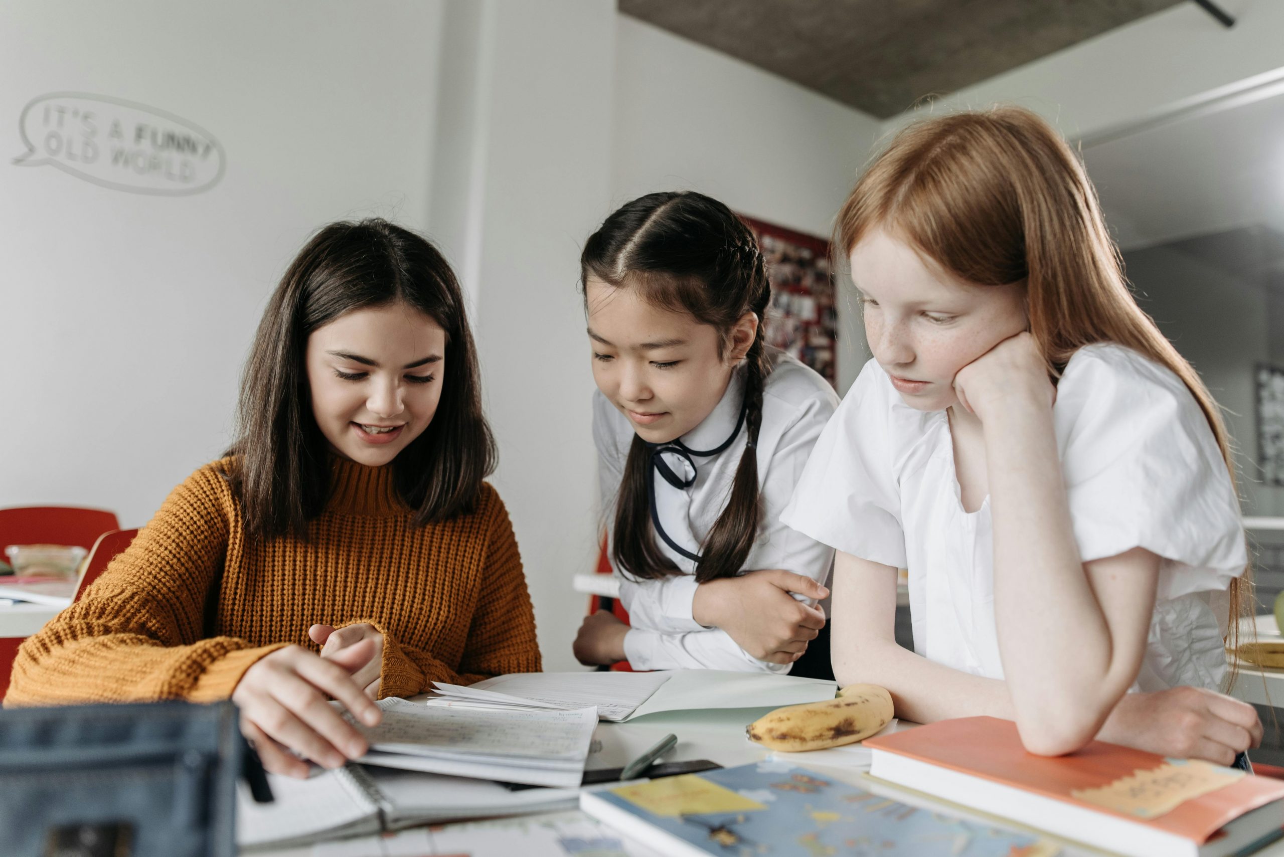 Tres estudiantes leyendo juntos un cuaderno y comentando el contenido en un entorno educativo.